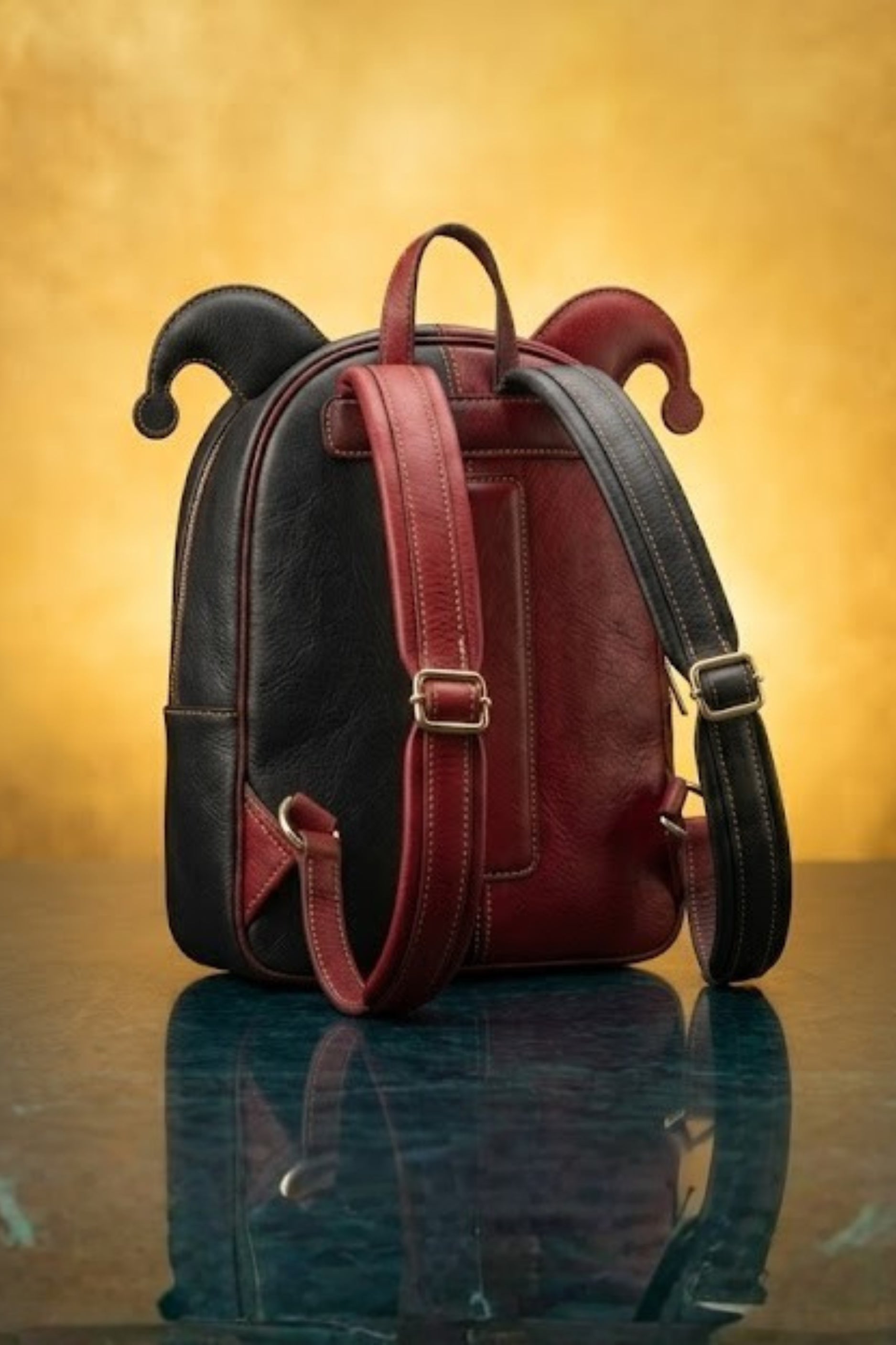 Back view of Harley Quinn inspired leather backpack showing black and red dual-tone exterior with jester horn ears, padded adjustable shoulder straps and gold hardware