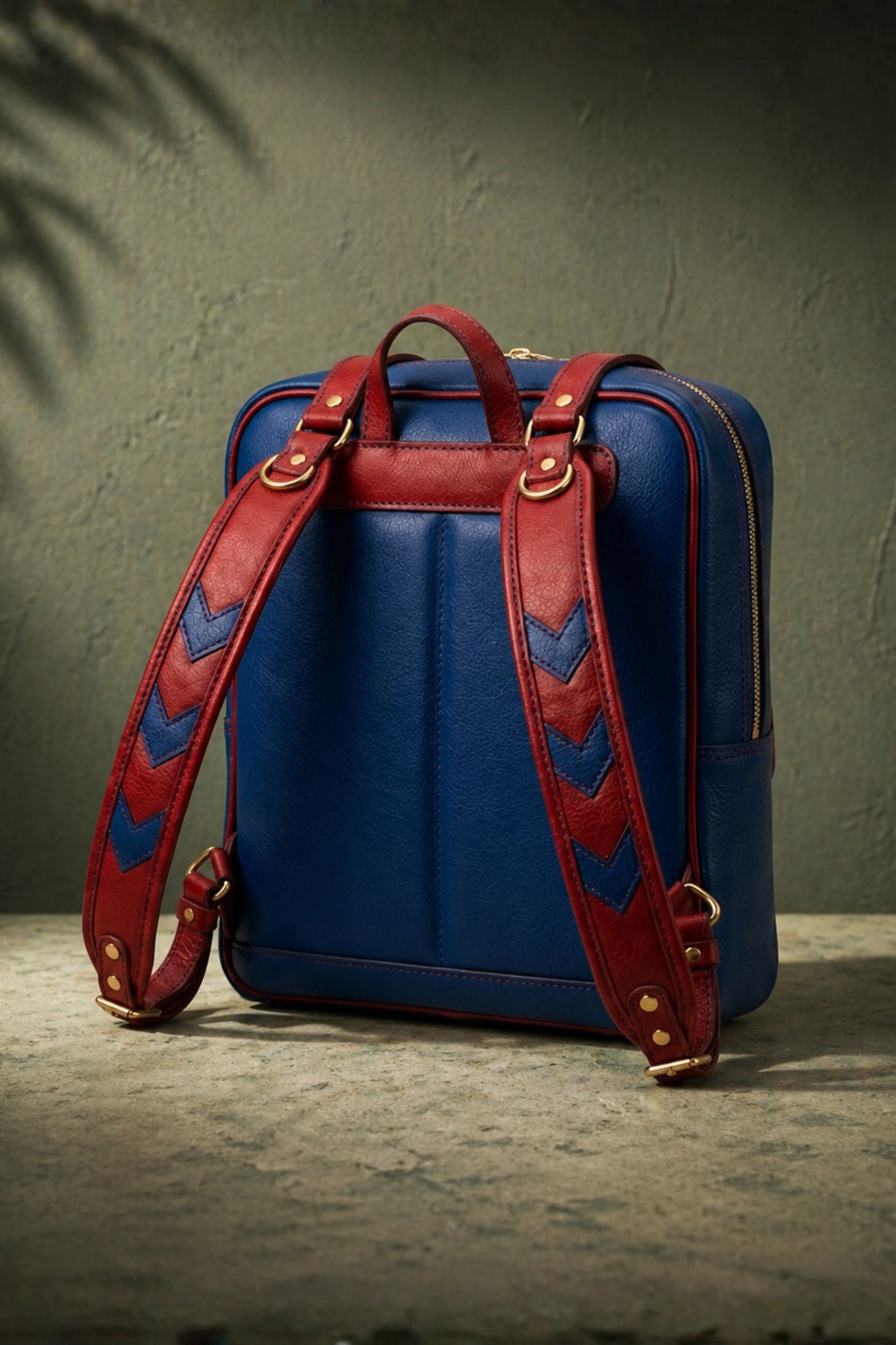 Mario inspired genuine leather backpack back view showing navy blue padded body with burgundy red chevron arrow patterned adjustable shoulder straps and gold hardware